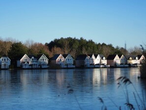 Une rangée de maisons au bord de l’eau, avec un lac paisible en premier plan.
