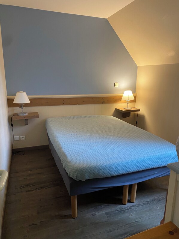 Une chambre à coucher avec un lit, deux lampes de chevet, une tête de lit en bois, un plancher en bois et un plafond en pente.