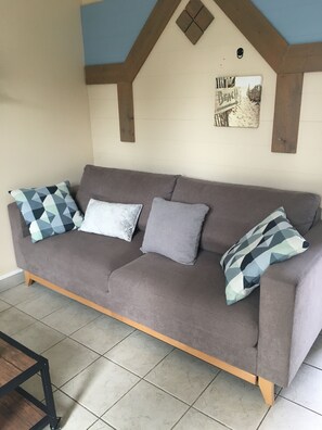 Un canapé gris agrémenté de coussins à motifs, un plancher en bois et un mur orné d’un panneau indiquant « Plage ».