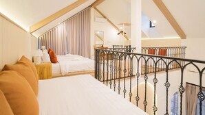 Ein Hotelzimmer mit schräg verlaufender Decke, einem Bett mit weißer Bettwäsche, einem Nachttisch mit Lampe und Blick auf den Balkon.