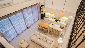 Ein großzügiger Wohnbereich mit einer Couch, Esstisch und Stühlen, eine Küche mit modernen Geräten sowie große Fenster mit leichtem Vorhang.