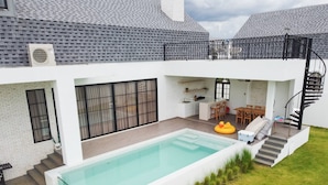 Ein modernes Haus mit Swimmingpool, Essbereich und einer Treppe, die zu einer oberen Ebene führt.