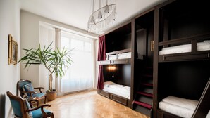 A room with a wooden herringbone floor, a large potted plant, a blue armchair, and a bunk bed with a red curtain. - Vienna Boutique - Premium Hostel (Vienna)