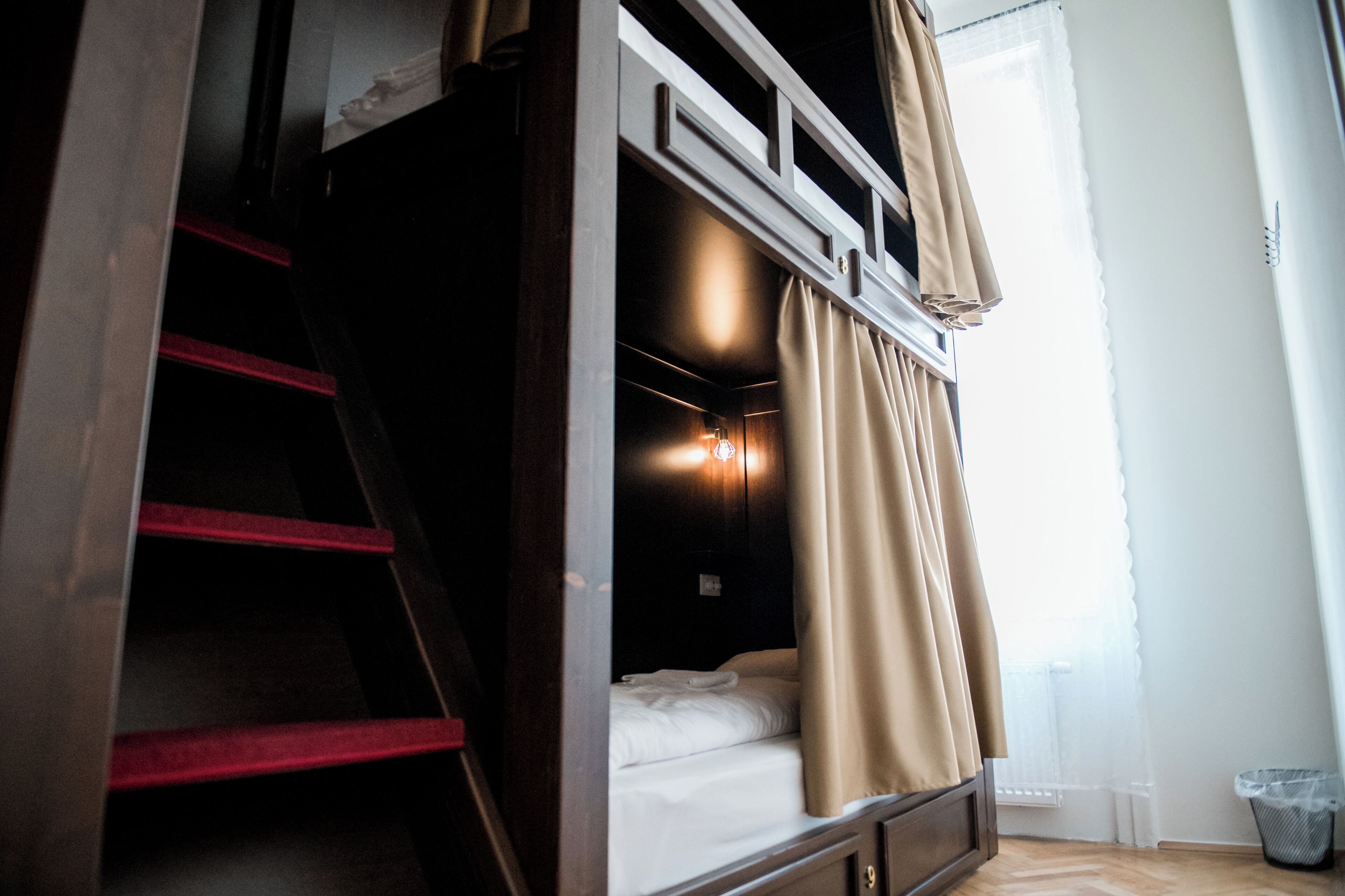 A bunk bed with a ladder, a small bedside table, and a window with curtains.