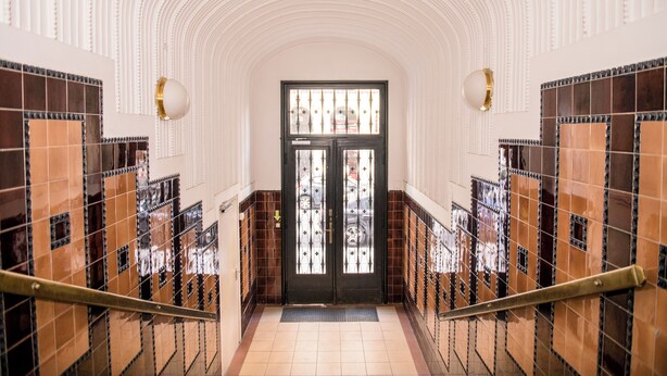 A hallway with a black door, tiled walls, and a staircase with metal railings. - Vienna Boutique - Premium Hostel (Vienna)