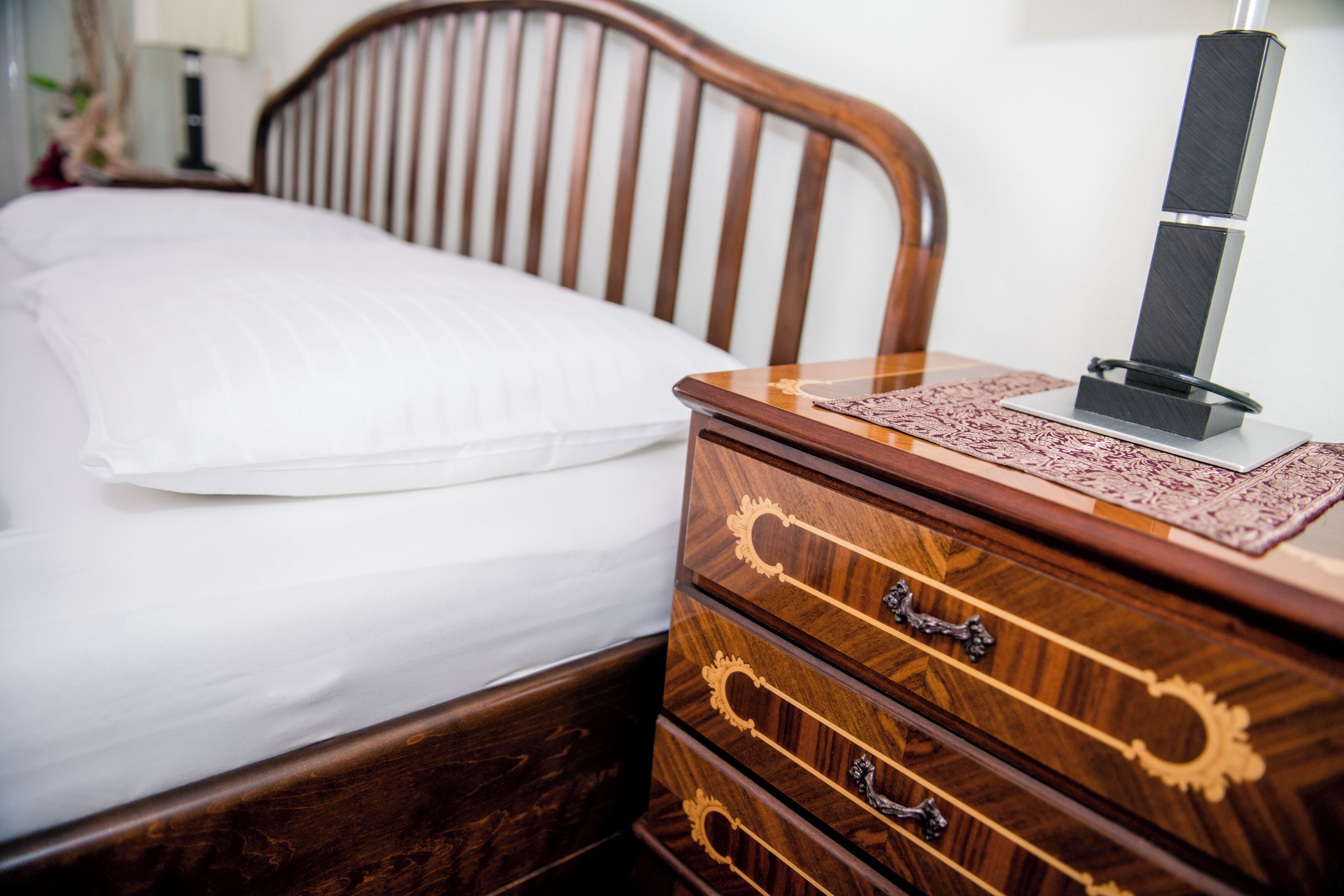 Una cama de madera con un colchón blanco y una mesita de noche de madera con cajones y una lámpara.