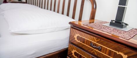 Una cama de madera con un colchón blanco y una mesita de noche de madera con cajones y una lámpara.