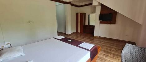 A hotel room with a large bed, a wooden floor, a television mounted on the wall, and a chair.