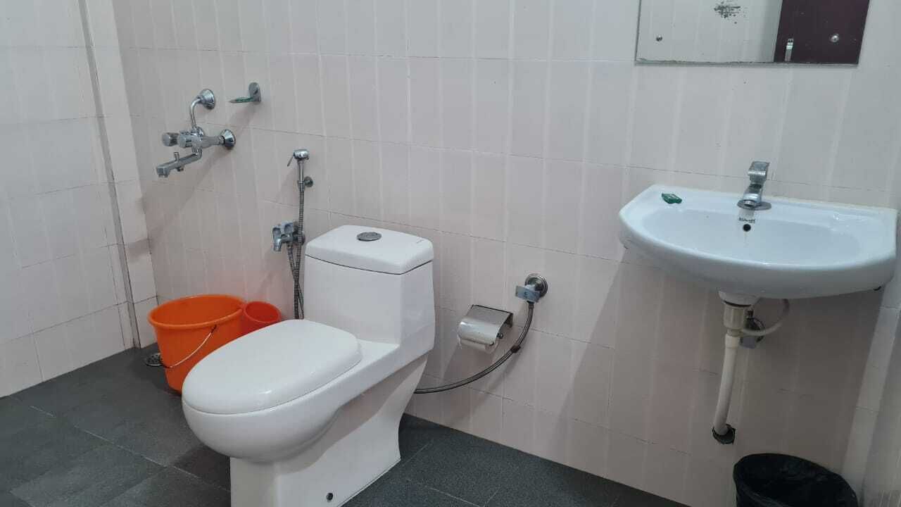 Une salle de bain équipée de toilettes, d’un bidet, d’un lavabo et de deux seaux orange.