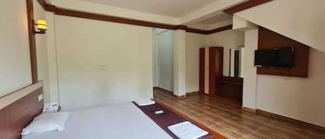 Una habitación de hotel con una cama grande, un cabecero de madera, una mesita de noche, un televisor de pantalla plana montado en la pared y suelo de madera.