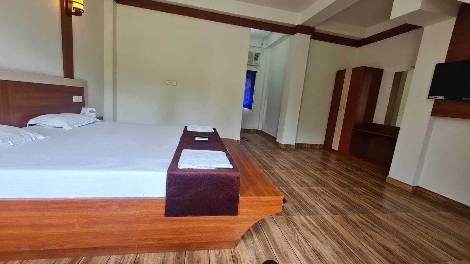 Habitación de hotel con cama de madera, una mesita con una toalla y un televisor montado en la pared.