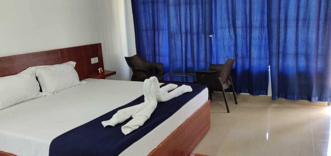 Una habitación de hotel con una cama grande, un cabecero de madera, una cortina azul y una pequeña mesa con dos sillas.
