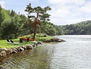 A lakeside setting with a grassy area, a canoe, and lounge chairs.
