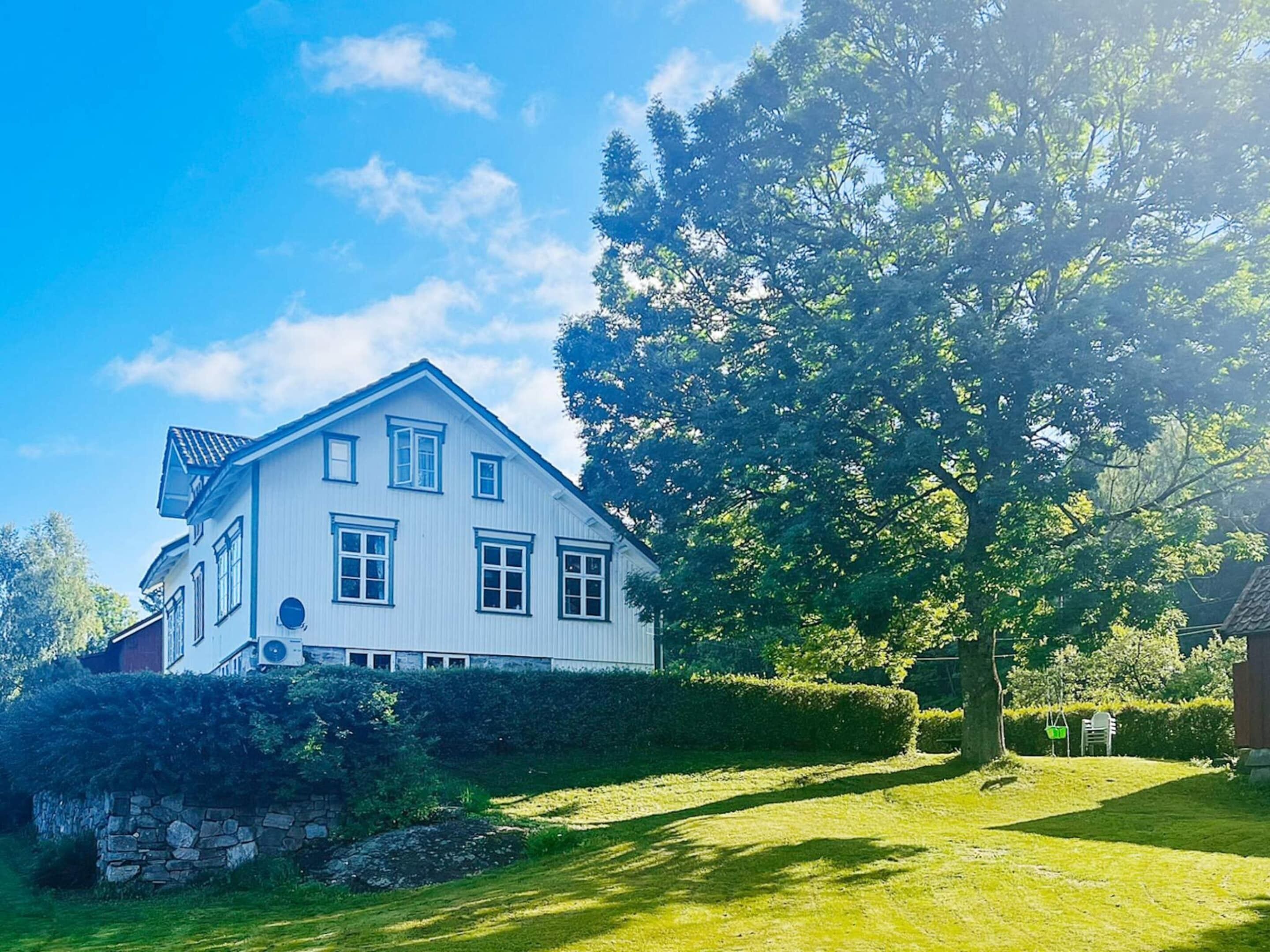 A white house with a stone wall, a large tree, and a clear blue sky.