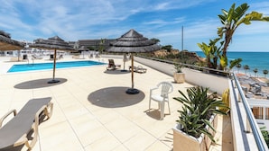 Un espace aménagé au bord de la piscine, avec des chaises longues, des parasols et une vue sur la mer.