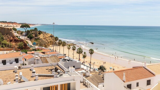 Une ville côtière aux bâtiments aux toits de tuiles rouges, avec une plage de sable fin et une mer d’un bleu limpide.