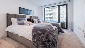 A bedroom with two beds, a large window, and a view of buildings outside. - LUX Riverside Apartment in Royal Wharf I Near LCY Airport/Canary Wharf/ExCel/O2 (Greater London)