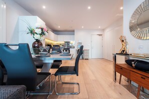 A modern dining area with a glass table, black chairs, and a decorative vase. - LUX Riverside Apartment in Royal Wharf I Near LCY Airport/Canary Wharf/ExCel/O2 (Greater London)