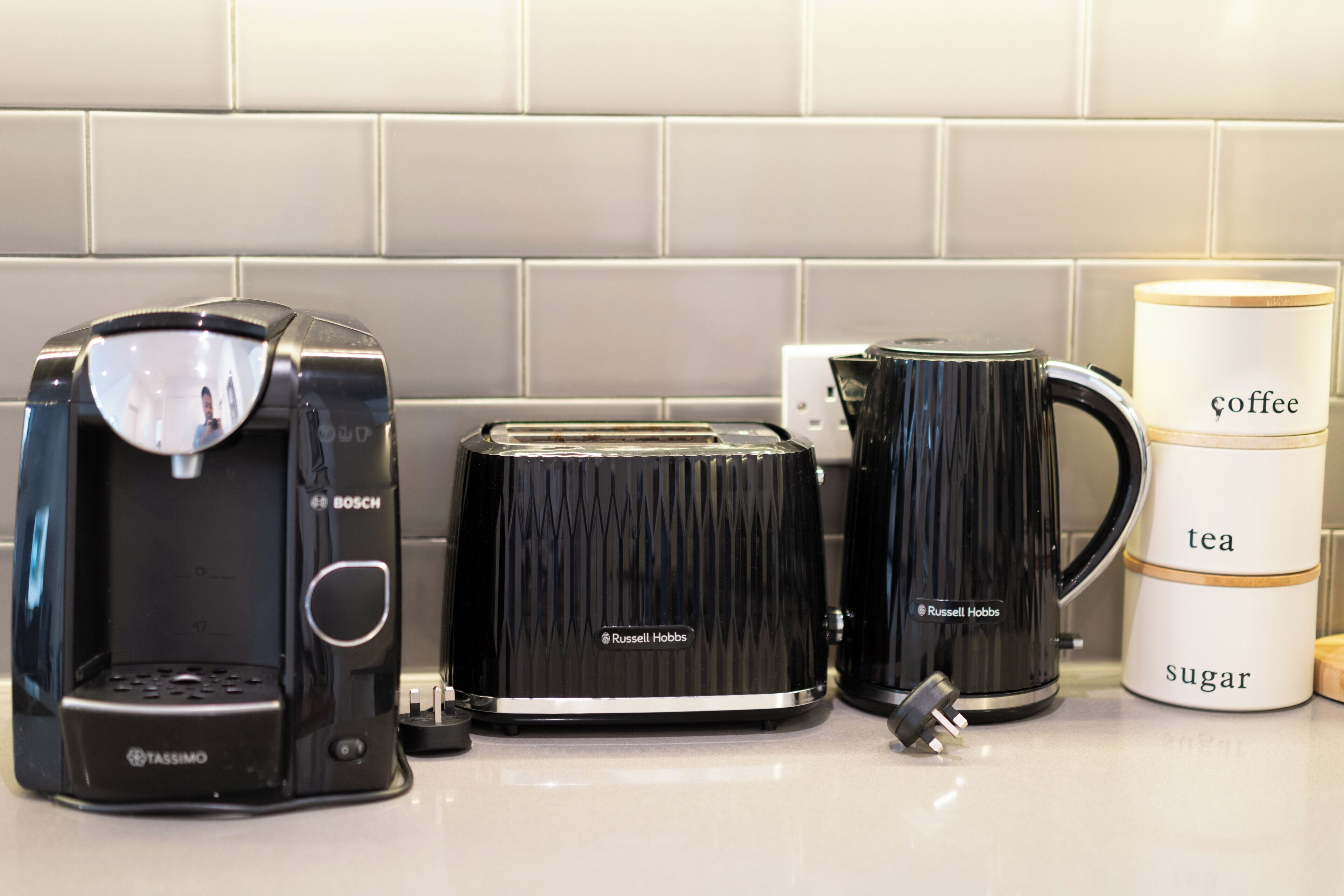 Une cuisine équipée d’une machine à café, d’un grille-pain, d’une bouilloire et d’une tasse sur laquelle sont indiqués les mots « café », « thé » et « sucre ».