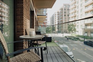 A balcony with wicker chairs and a table, overlooking a street with cars and buildings.