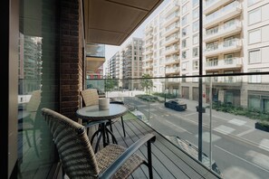 A balcony with wicker furniture, a glass table, and a view of a multi-story building with balconies. - LUX Riverside Apartment in Royal Wharf I Near LCY Airport/Canary Wharf/ExCel/O2 (Greater London)