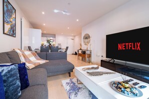 A modern living room with a grey sofa, a white coffee table, and a flat-screen TV displaying 'NETFLIX'.