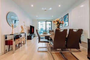 A modern dining area with a glass table, brown chairs, a large mirror, and a vase of flowers.