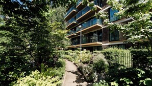 A pathway leading to a multi-story building surrounded by dense greenery. - LUX Riverside Apartment in Royal Wharf I Near LCY Airport/Canary Wharf/ExCel/O2 (Greater London)