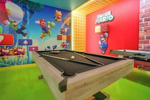 Una mesa de billar con una pared con temática de Super Mario y una pared de ladrillo.