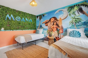 Una habitación con un mural de Moana, dos camas, una pared verde con las letras 'MOANA' y una escena de playa tropical.