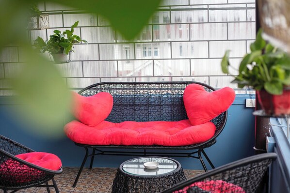 A balcony with a wicker chair and cushions, a small table, and potted plants. - Little View Homestay (Sa Pa)