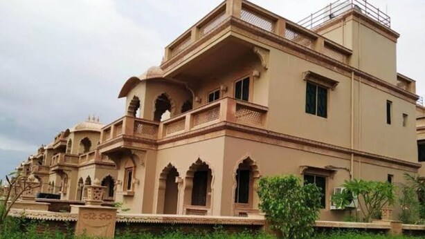 A traditional building with multiple balconies and arched windows, surrounded by greenery. - Rajvada bounglos (Bhuj)