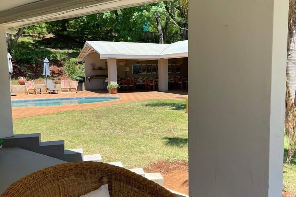 Una silla de mimbre con un cojín blanco, una mesa de madera y vistas a una piscina y un área de estar al aire libre.