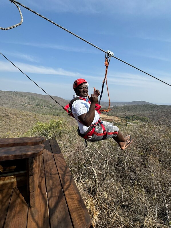 A person on a zip line with a wooden platform and a view of a hilly landscape. - Madi a Thavha Mountain Lodge (Louis Trichardt)