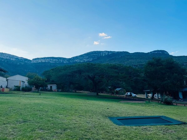 A grassy outdoor area with a trampoline, trees, and a building in the background. - Madi a Thavha Mountain Lodge (Louis Trichardt)