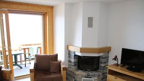 Uma sala de estar aconchegante com lareira de pedra, uma televisão em um suporte de madeira e uma área de jantar com mesa e cadeiras.