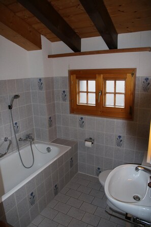 Un baño con bañera, lavamanos y ventana con persianas de madera.