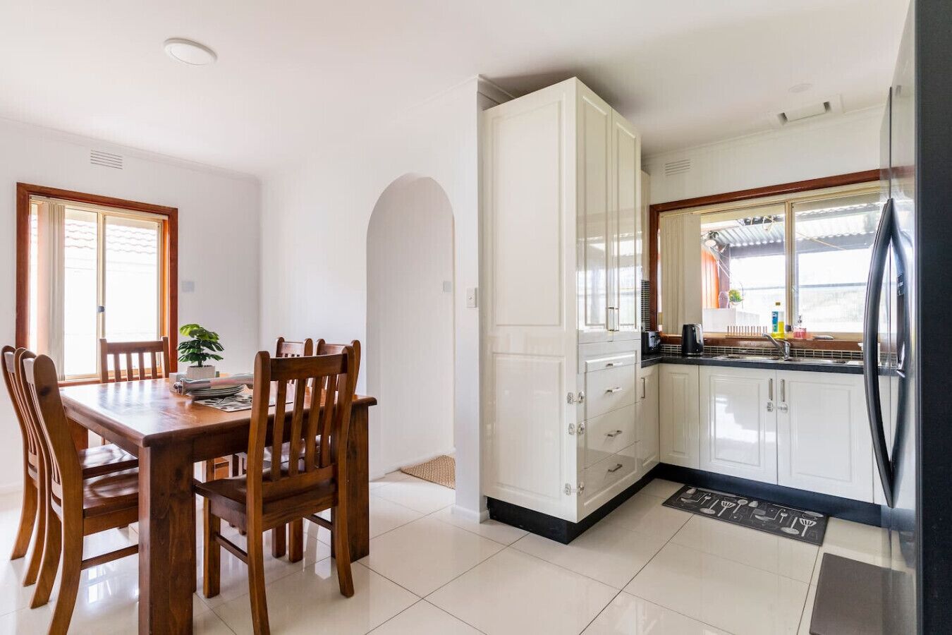 A compact kitchen with white cabinets, a dining table with chairs, and a refrigerator.