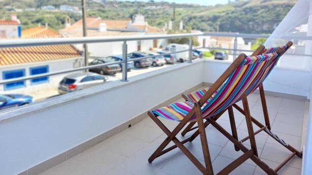 Un balcon avec un fauteuil suspendu à rayures, une vue sur les voitures garées et des bâtiments en arrière-plan.