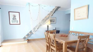 Un coin repas avec une table et des chaises en bois, une lampe et un escalier muni d’un filet de sécurité.