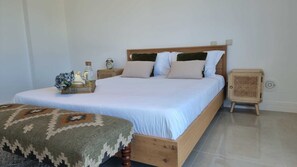 Un letto rifatto con cura, una testiera in legno, un comodino con una lampada e un tavolino di rattan intrecciato.