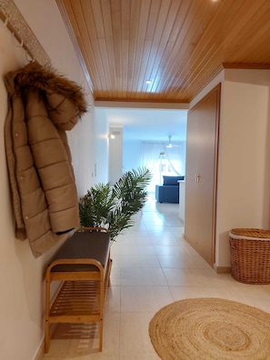 A hallway with a bench, a potted plant, a wicker basket, and a door leading to another room.
