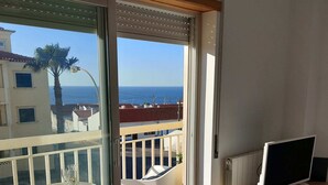 Un balcon avec une porte vitrée, un téléviseur posé sur un meuble en bois et une table avec des chaises.