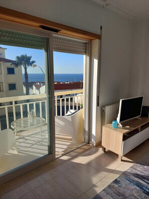 Un balcone con una porta vetrata, una TV su un mobile in legno e un tavolo con sedie.