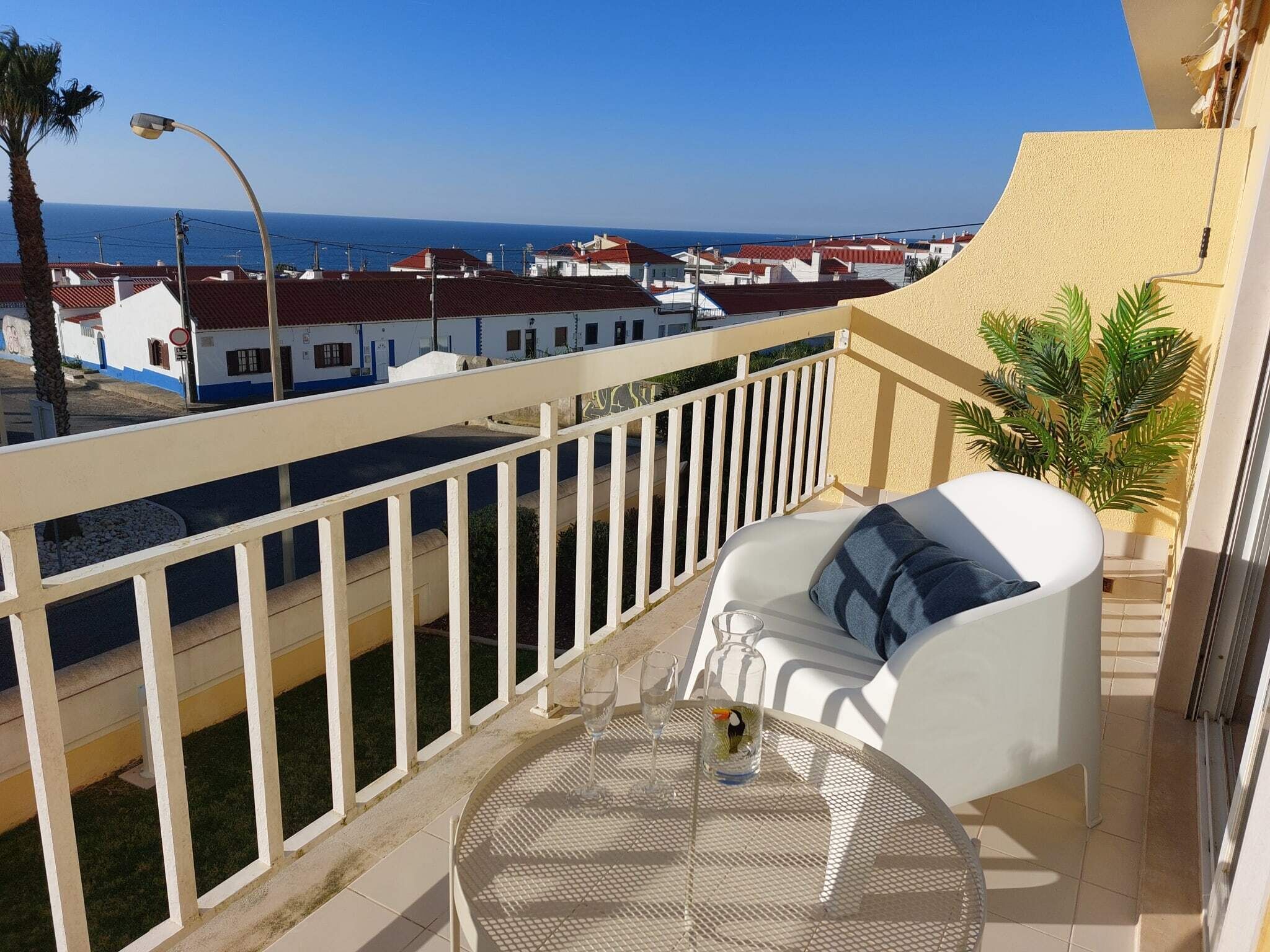 A balcony with a white chair, a round table, and a small plant.