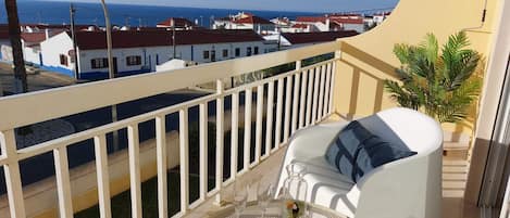 Un balcon avec une chaise blanche, une table ronde et une petite plante.