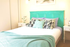 A bed with a patterned bedspread, a teal headboard, and multiple pillows with various designs.