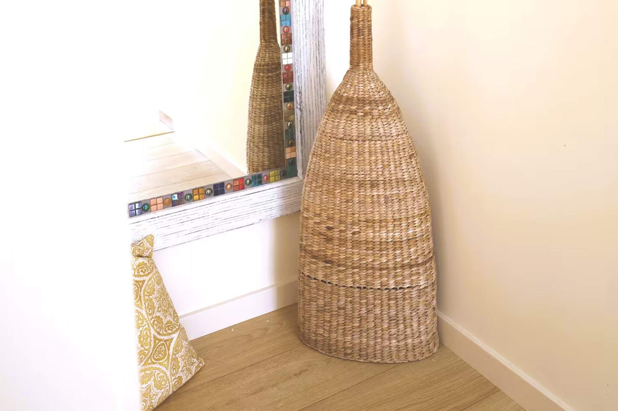 Un coin de pièce avec un panier en osier et un coussin à motifs appuyé contre un mur.