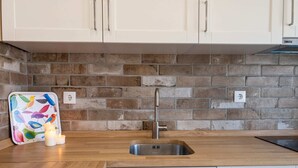 A kitchen with a brick backsplash, a stainless steel sink, and white cabinets. - Grandchildren's House (Mafra)