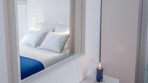 A modern room with a large mirror, a bedside table, and a bed with white bedding. - Grandchildren's House (Mafra)